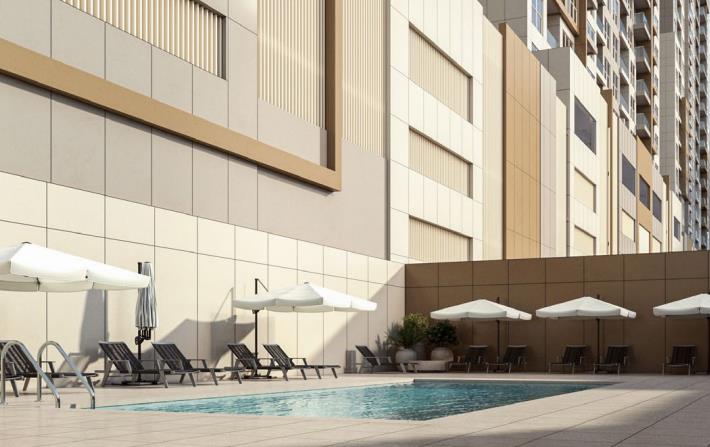 Swimming pool area at Ajman One Phase 2, surrounded by lounge chairs and umbrellas for relaxation.